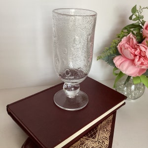 May include: A clear glass goblet with a textured surface and a round base. The goblet has a bubbled design.