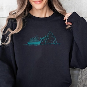 May include: Black sweatshirt with a teal graphic of a ship, iceberg, and the word "Beep!". The sweatshirt is a solid black color and has a crew neck. The graphic is a simple line drawing style.