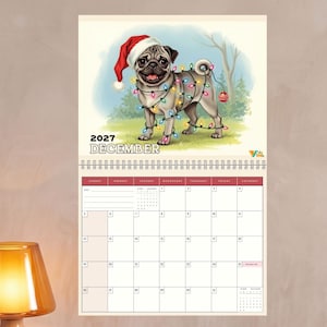 May include: A wall calendar for December 2027 featuring an illustration of a pug wearing a red Santa hat and wrapped in colorful Christmas string lights. The calendar grid below the image displays the days of the month with a white background.