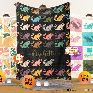 May include: Three rectangular blankets featuring distinct designs. The left blanket has a cream background with yellow raccoons and floral patterns. The center black blanket displays repeating colorful raccoons and the name elizabeth. The right blanket has a grid pattern with various colored raccoons and the name elizabeth.