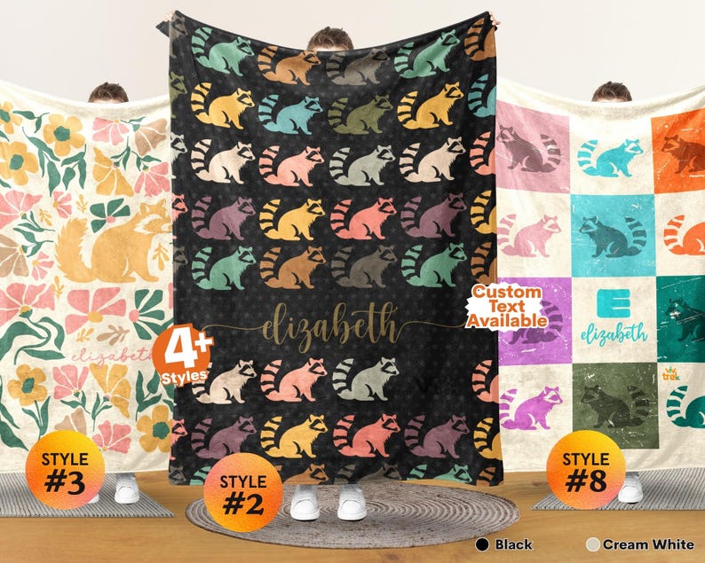 May include: Three rectangular blankets featuring distinct designs. The left blanket has a cream background with yellow raccoons and floral patterns. The center black blanket displays repeating colorful raccoons and the name elizabeth. The right blanket has a grid pattern with various colored raccoons and the name elizabeth.