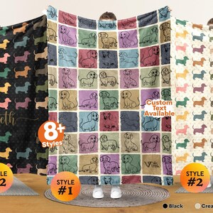 May include: Three soft blankets featuring repeating dachshund patterns. The left blanket is black with colorful dog silhouettes and the name Elizabeth. The center blanket has a grid of colorful squares with dachshund illustrations. The right blanket is cream white.