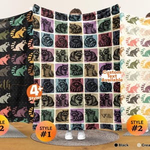 May include: Three fleece blankets featuring raccoon patterns. The left blanket is black with colorful raccoons and the name Elizabeth. The center blanket has a grid of raccoons in squares. The right blanket is cream white with colorful raccoons.