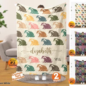 May include: A cream white throw blanket featuring a repeating pattern of illustrated badgers in various colors including brown, green, yellow, pink, and purple. The center displays the name elizabeth in cursive script and the logo viv trek.