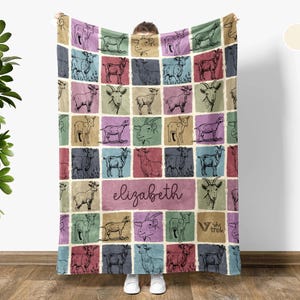 May include: Cream white blanket featuring a grid pattern of goat illustrations in various colors. The blanket has a personalized name, "Elizabeth", in a cursive font. The blanket is made of a soft material.