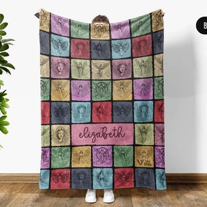 May include: A rectangular throw blanket featuring a grid of colorful squares, each containing a black line-art illustration of an angel. A central horizontal rectangle displays the name elizabeth in cursive script. The background colors include pink, blue, green, yellow, and purple.