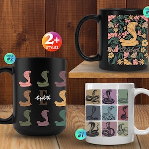 Op de afbeelding: Drie keramische mokken met cobra-illustraties. Eén zwarte mok toont een raster van gekleurde cobra's en de naam Elizabeth. Een andere zwarte mok toont een enkele cobra tussen bloemmotieven en de naam Elizabeth. Een witte mok toont een raster van negen cobra-illustraties.
