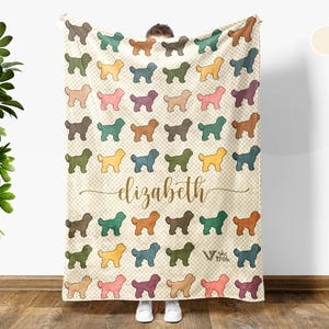 May include: Cream-colored blanket featuring a repeating pattern of colorful dog silhouettes. The blanket has the name "Elizabeth" in gold script. The blanket is made of a soft material and is perfect for snuggling.