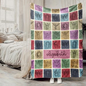 May include: A rectangular throw blanket featuring a grid of colorful squares, each displaying a unique line-art illustration of an angel. The center square contains the name elizabeth in cursive script, and the bottom right corner features a small logo.
