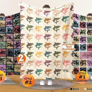 May include: Three rectangular blankets featuring shark patterns. The left blanket has a grid of colorful shark illustrations on a dark background. The center blanket is cream white with repeating shark silhouettes. The right blanket shows a grid with the name elizabeth.