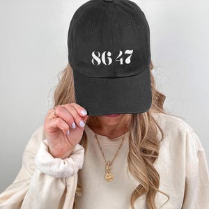 Może przedstawiać: Czarna czapka bejsbol&oacute;wka z białymi cyframi "8647" nadrukowanymi z przodu. Czapka ma zakrzywiony daszek i klasyczny, swobodny styl. Kapelusz jest wykonany z miękkiego materiału.