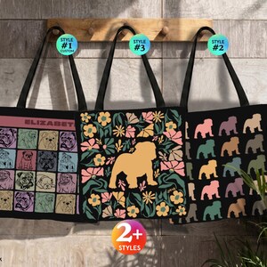 Könnte beinhalten: Drei schwarze Tragetaschen hängen an einer Holzleiste. Die linke Tasche zeigt ein Raster aus sechzehn Bulldoggen-Illustrationen mit dem Namen ELIZABETH. Die mittlere Tasche zeigt eine große beige Bulldoggen-Silhouette, umgeben von bunten Blumen. Die rechte Tasche hat ein wiederkehrendes Muster aus Bulldoggen-Silhouetten in verschiedenen Farben.