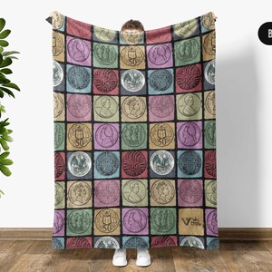 May include: A colorful blanket featuring a repeating pattern of vintage coin illustrations in various colors. The blanket is held up, displaying the design. The background is a neutral color.