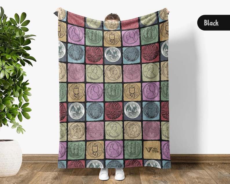 May include: A colorful blanket featuring a repeating pattern of vintage coin illustrations in various colors. The blanket is held up, displaying the design. The background is a neutral color.