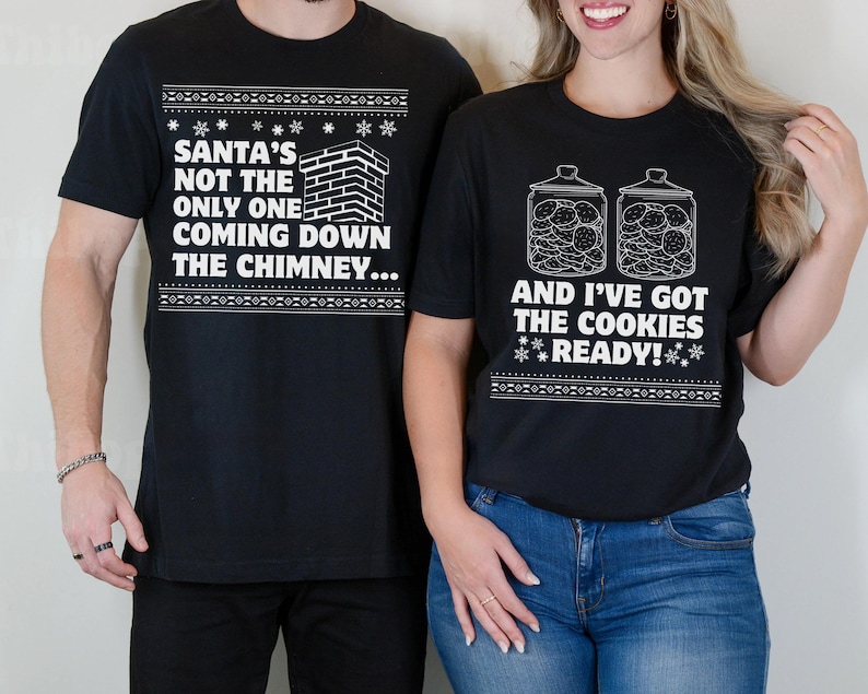 K&ouml;nnte beinhalten: Zwei schwarze T-Shirts mit wei&szlig;em Text und Grafiken. Das erste Shirt sagt "Santa's not the only one coming down the chimney..." Das zweite Shirt sagt "And I've got the cookies ready!" mit einer Grafik von zwei Keksdosen.