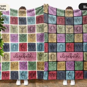 May include: Two rectangular blankets featuring a grid of squares with angel illustrations in various colors. One blanket has a cream white background, the other black. Both display the name elizabeth in a central rectangular panel in script font.