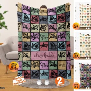 May include: A rectangular throw blanket featuring a grid pattern of various shark illustrations in shades of blue, pink, yellow, and black. The center includes a rectangular panel with the name elizabeth in cursive script and a logo for viv trek.