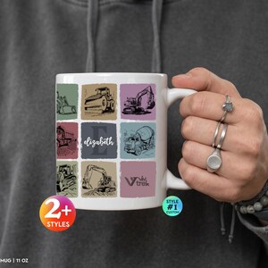 May include: A white 11 oz ceramic mug featuring a grid of construction vehicle illustrations, including a bulldozer, excavator, and cement mixer. The design includes a central square with the name Elizabeth and a logo reading Viv Trek.