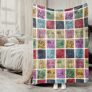May include: A colorful throw blanket featuring a grid pattern of various dog illustrations in black outlines. Each dog is set within a square of a different color, including red, blue, green, and purple. The blanket is displayed in a bedroom setting.