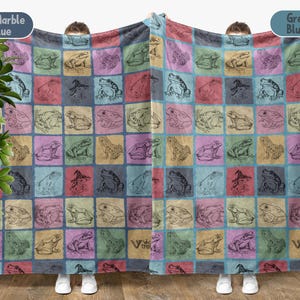 Puede incluir: Una manta de felpa suave y mullida con un patr&oacute;n repetido de ranas en varias poses. La manta est&aacute; en un esquema de color azul y rosa con un sutil efecto de m&aacute;rmol. El texto "Marble Blue" y "Greyish Blue" est&aacute; impreso en las esquinas superiores de la manta.