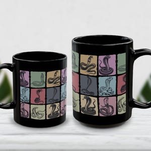 May include: Two black ceramic mugs with a colourful snake pattern. The design features various snake illustrations in a grid of pastel-coloured squares. The mugs have a glossy finish and a curved handle.