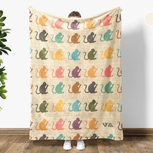 May include: A cream white throw blanket with a repeating pattern of colorful monkey silhouettes. The blanket is made of a soft, plush material and is perfect for cuddling up on the couch.