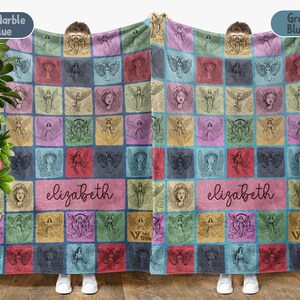 May include: A rectangular blanket featuring a grid of colorful squares, each containing a line-art illustration of an angel. A central rectangular panel displays the name "elizabeth" in a cursive script. The blanket displays various shades of blue, pink, yellow, and green.