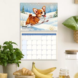 May include: A 2026 January wall calendar featuring a cartoon corgi dog running in a snowy winter scene. The calendar has a spiral binding and a grid layout for each day of the month.