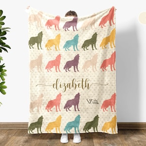 May include: A cream white fleece blanket with a repeating pattern of colorful wolf silhouettes. The blanket has the name "elizabeth" written in brown cursive script.