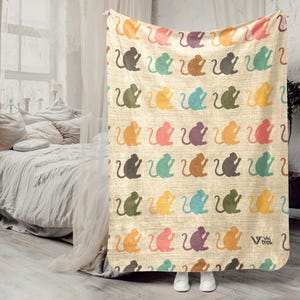 May include: A beige throw blanket with a repeating pattern of colorful monkeys sitting in a row. The monkeys are in various colors, including red, orange, yellow, green, blue, and purple. The blanket has the text "V-trek" in the bottom right corner.