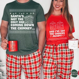 K&ouml;nnte beinhalten: Ein Paar tr&auml;gt passende Weihnachtspyjamas. Der Mann tr&auml;gt ein gr&uuml;nes T-Shirt mit dem Text "Santa's not the only one coming down the chimney..." und eine rot-gr&uuml;ne karierte Schlafhose. Die Frau tr&auml;gt ein rotes T-Shirt mit dem Text "And I've got the cookies ready!" und eine rot-gr&uuml;ne karierte Schlafhose.