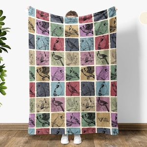 May include: A cream white throw blanket with a colorful pattern of birds in a grid design. The birds are drawn in a vintage style and include cardinals, bluebirds, and other songbirds.