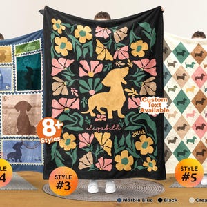 May include: Three rectangular blankets featuring dachshund designs. The left blanket has blue postage stamp motifs with dachshund silhouettes. The center black blanket displays a large yellow dachshund surrounded by pink and yellow flowers with the text elizabeth. The right blanket has a cream-colored diamond pattern with small dachshunds.