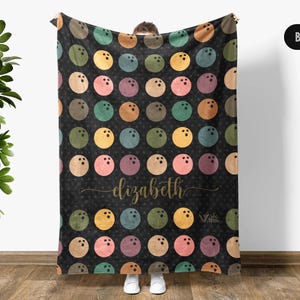 May include: A black fleece blanket with a pattern of colorful bowling balls. The blanket has the name "elizabeth" printed in gold lettering.