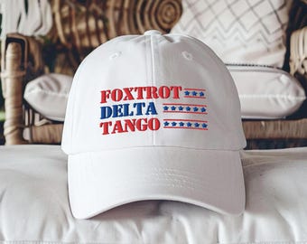 May include: White baseball cap with red, white, and blue embroidered text that reads "FOXTROT DELTA TANGO" and a row of stars.