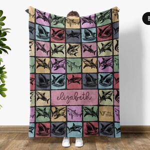 Może przedstawiać: Kolorowy koc z powtarzającym się wzorem ilustracji rekin&oacute;w. Koc ma spersonalizowaną sekcję z imieniem "Elizabeth" w kursywie. Tło to patchwork kwadrat&oacute;w w pastelowych odcieniach.
