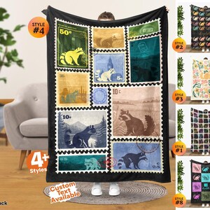 May include: A black fleece blanket featuring a collage of vintage-style postage stamp graphics, each displaying a raccoon illustration in various colors and settings, with numerical values like 50c, 10c, 35c, and 55c printed on the individual stamp designs.