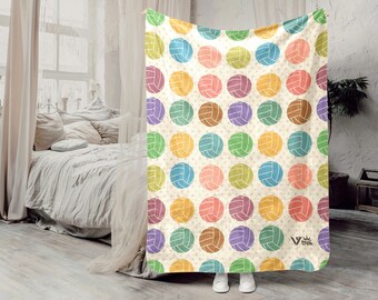 May include: A cream-colored fleece blanket featuring a repeating pattern of colorful volleyballs in shades of blue, yellow, green, pink, purple, and brown. The fabric is decorated with small star shapes and includes the Viv Trek logo in the corner.