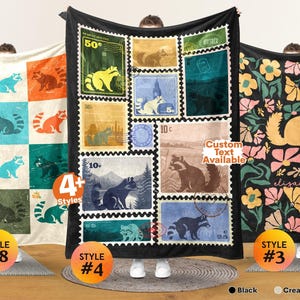 May include: Three rectangular blankets featuring raccoon designs. The left blanket has a grid of colorful raccoons. The center black blanket displays a collage of vintage-style postage stamps with raccoon illustrations. The right blanket shows a floral pattern with a central raccoon and the name Elizabeth.