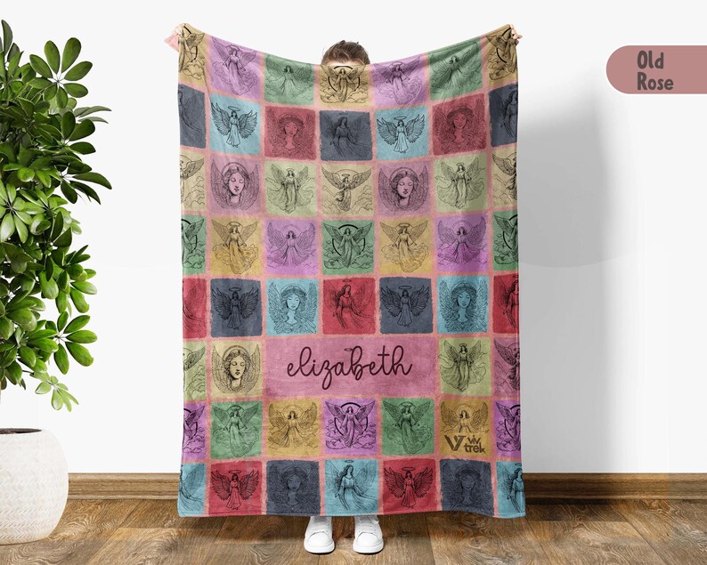 May include: A rectangular fleece blanket featuring a grid of squares with various angel illustrations in shades of pink, blue, green, and yellow. The center square displays the name elizabeth in a dark script font. The blanket has a soft texture.