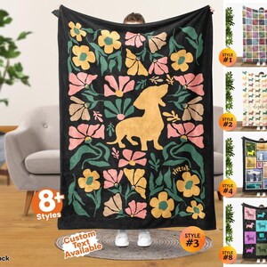 May include: A black rectangular throw blanket featuring a central golden yellow dachshund silhouette surrounded by a repeating pattern of stylized pink, yellow, and green flowers. The word vivtrek is printed in small yellow letters near the bottom right.