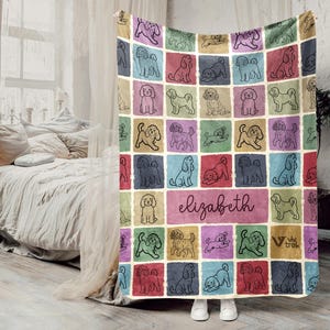 May include: A colorful throw blanket featuring a grid pattern of illustrated dogs in various poses, set against a backdrop of pastel squares. The name "Elizabeth" is written in cursive on a pink rectangle. The blanket is displayed indoors.
