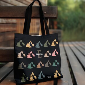 May include: Black tote bag featuring a pattern of colorful construction excavators. The bag has black handles and the name "Elizabeth" with the initial "E" in the center. The bag is made of a durable material.