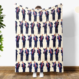 May include: Cream white blanket featuring a repeating pattern of a man in a blue suit and red tie. The blanket is held up by a person wearing white shoes. The blanket is cream white.
