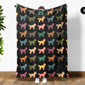 May include: Black blanket with a repeating pattern of colorful dog silhouettes. The dogs are in shades of yellow, pink, green, orange, and brown. The blanket is held up against a white wall.