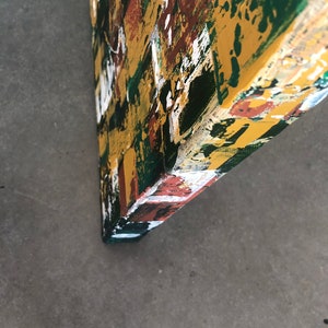 Op de afbeelding: Hoek van een abstract kunstwerk, met een levendige mix van kleuren. Het kunstwerk heeft gedurfde penseelstreken van geel, groen, wit en bruin, waardoor een textuur ontstaat. De randen zijn donkergroen geschilderd.