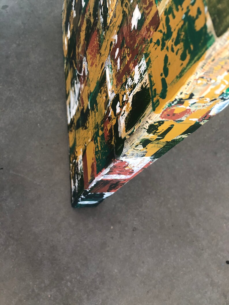 Op de afbeelding: Hoek van een abstract kunstwerk, met een levendige mix van kleuren. Het kunstwerk heeft gedurfde penseelstreken van geel, groen, wit en bruin, waardoor een textuur ontstaat. De randen zijn donkergroen geschilderd.