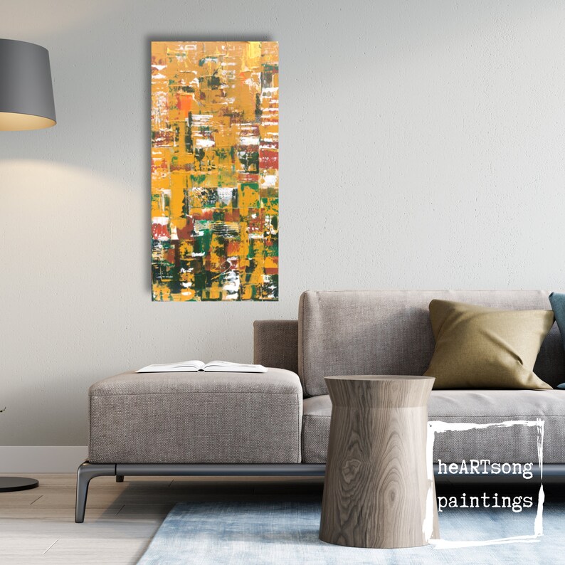 Op de afbeelding: Abstract schilderij met een rechthoekige vorm, met een textuur oppervlak met een mix van kleuren waaronder geel, oranje, groen, rood en wit. Het schilderij wordt op een witte muur getoond. Het schilderij is gesigneerd "heartSong paintings".