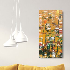 Op de afbeelding: Abstracte kunstschilderij met een textuuroppervlak. Het kunstwerk toont een mix van kleuren, waaronder goud, geel, groen, rood en wit, gerangschikt in een rechthoekige compositie. Het schilderij wordt op een witte muur getoond.