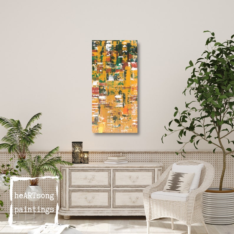 Op de afbeelding: Abstracte kunstschilderij met een verticaal rechthoekig formaat. Het kunstwerk heeft een textuur met een mix van kleuren, waaronder geel, groen, wit en rood. Het schilderij wordt tentoongesteld aan een muur in een kamer met een neutraal kleurenpalet. De tekst "heartSong paintings" is zichtbaar.